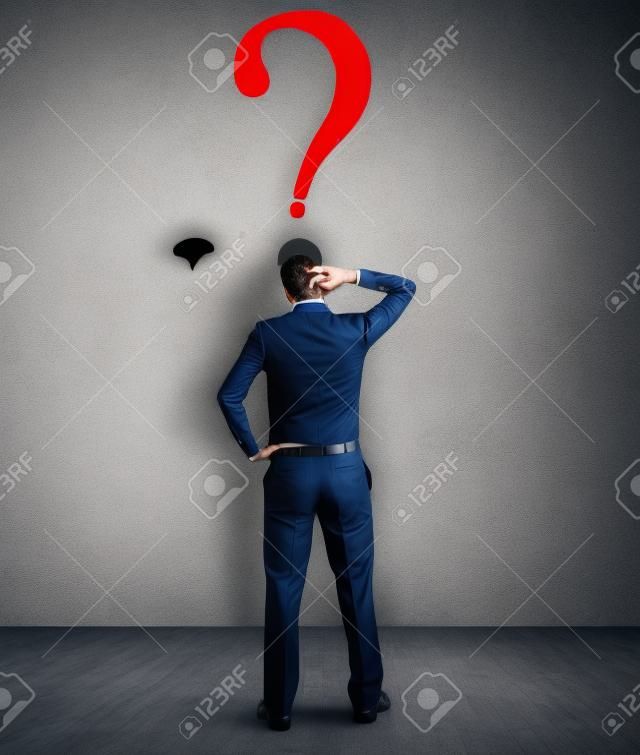 Confused businessman looking at Fragezeichen in der Wand
