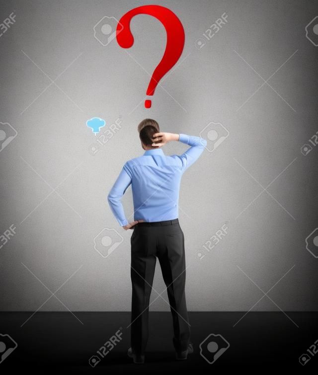 Confused businessman looking at question mark in the wall