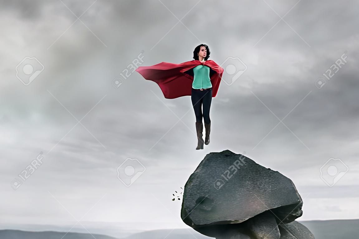 Business woman as a super hero on the peak of a mountain