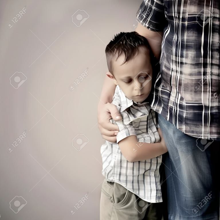 грустно сын обнимает своего отца возле стены в дневное время