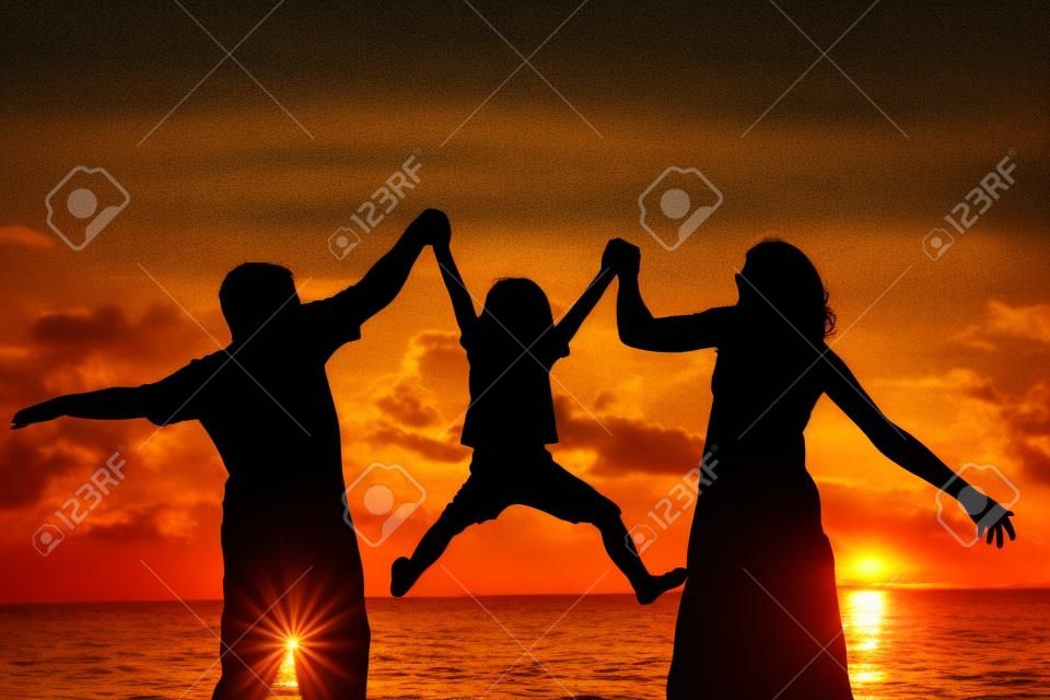 Silueta de la familia feliz que juega en la playa en la puesta del sol. Concepto de la familia.