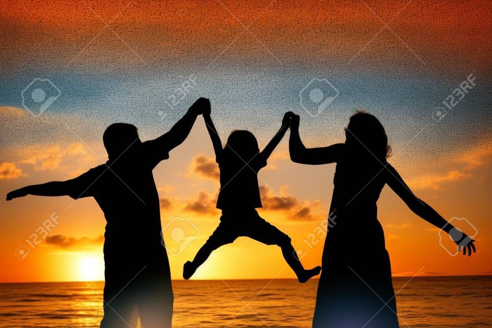 Silhueta de família feliz que joga na praia na hora do pôr do sol. Conceito de família amigável.