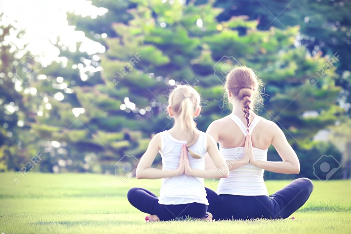 母親和女兒做瑜伽練習在草地上，在公園，在一天的時間