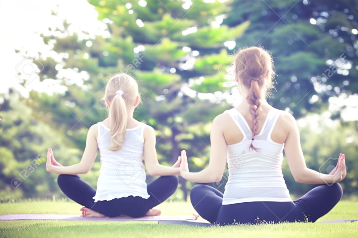 Мать и дочь, делать упражнения йоги на траве в парке в дневное время