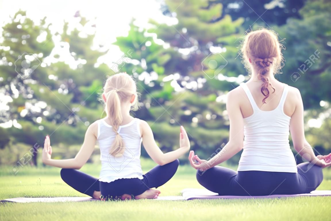 Мать и дочь, делать упражнения йоги на траве в парке в дневное время