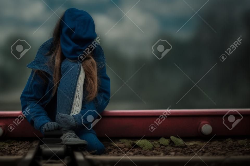 Portret młodej smutnej dziewczyny siedzącej na zewnątrz na kolei w pojęciu smutku w ciągu dnia
