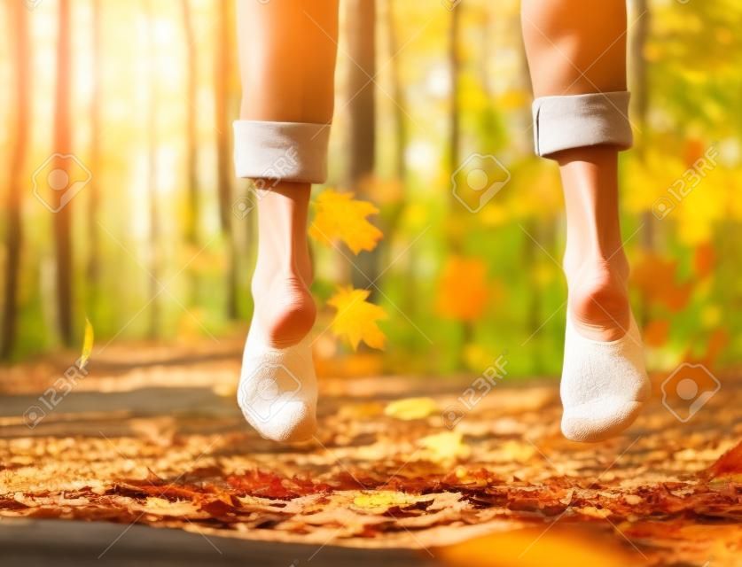 女性健康的腿或脚赤脚和脚跟和脚趾跳在木材上阳光明媚的户外在秋季森林与季节树叶在自然背景为自由的象征。