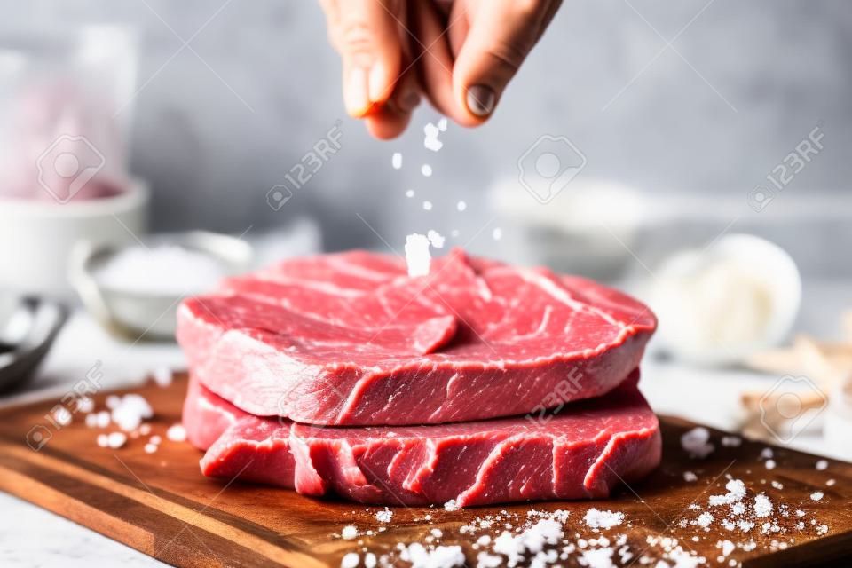 Espolvorear sal a mano sobre carne fresca de res cruda en una tabla para cortar