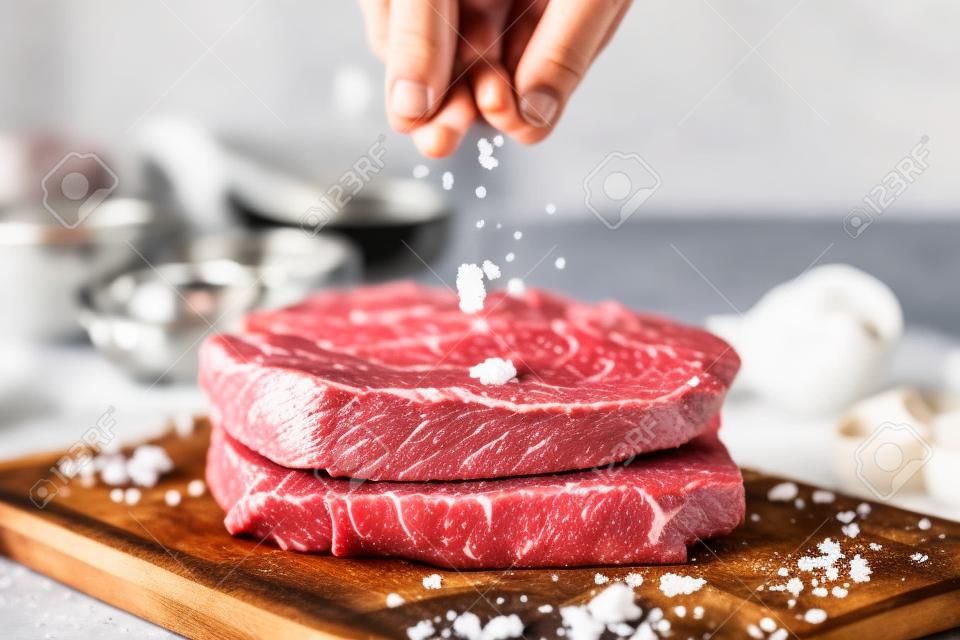 Hand bestrooiend zout op vers rauw rundvlees op een snijplank