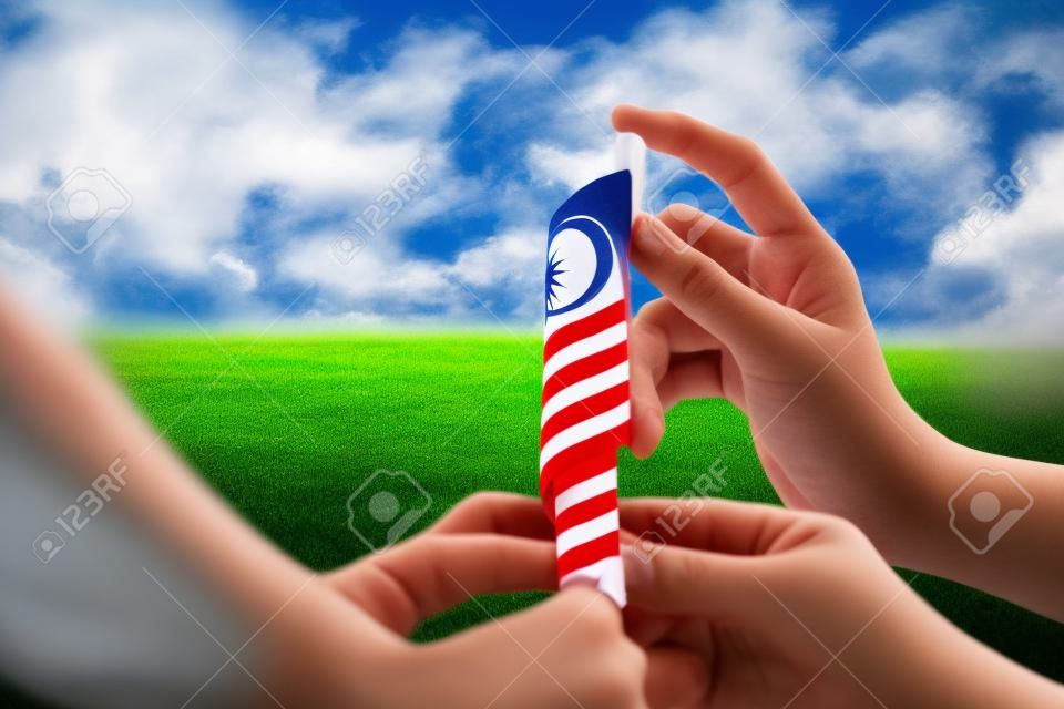Independence Day concept - Kids' hands holding Malaysian flag on a field.
