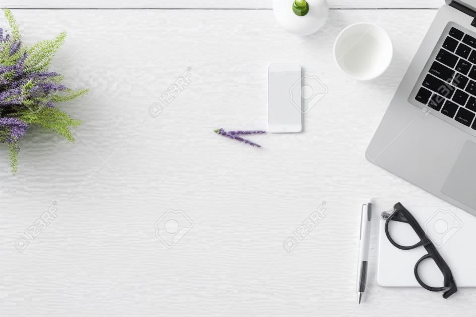 白色辦公檯桌上配有筆記本電腦，智能手機，筆，薰衣草，繩索和玻璃。頂視圖與副本空間，平躺。