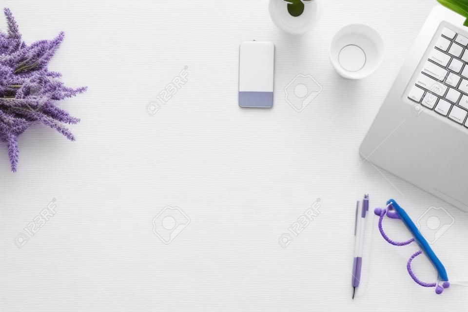 Mesa de escritorio de oficina blanca con laptop, teléfono inteligente, bolígrafo, lavanda, cuerda y vidrio. Vista superior con espacio de copia, plano.