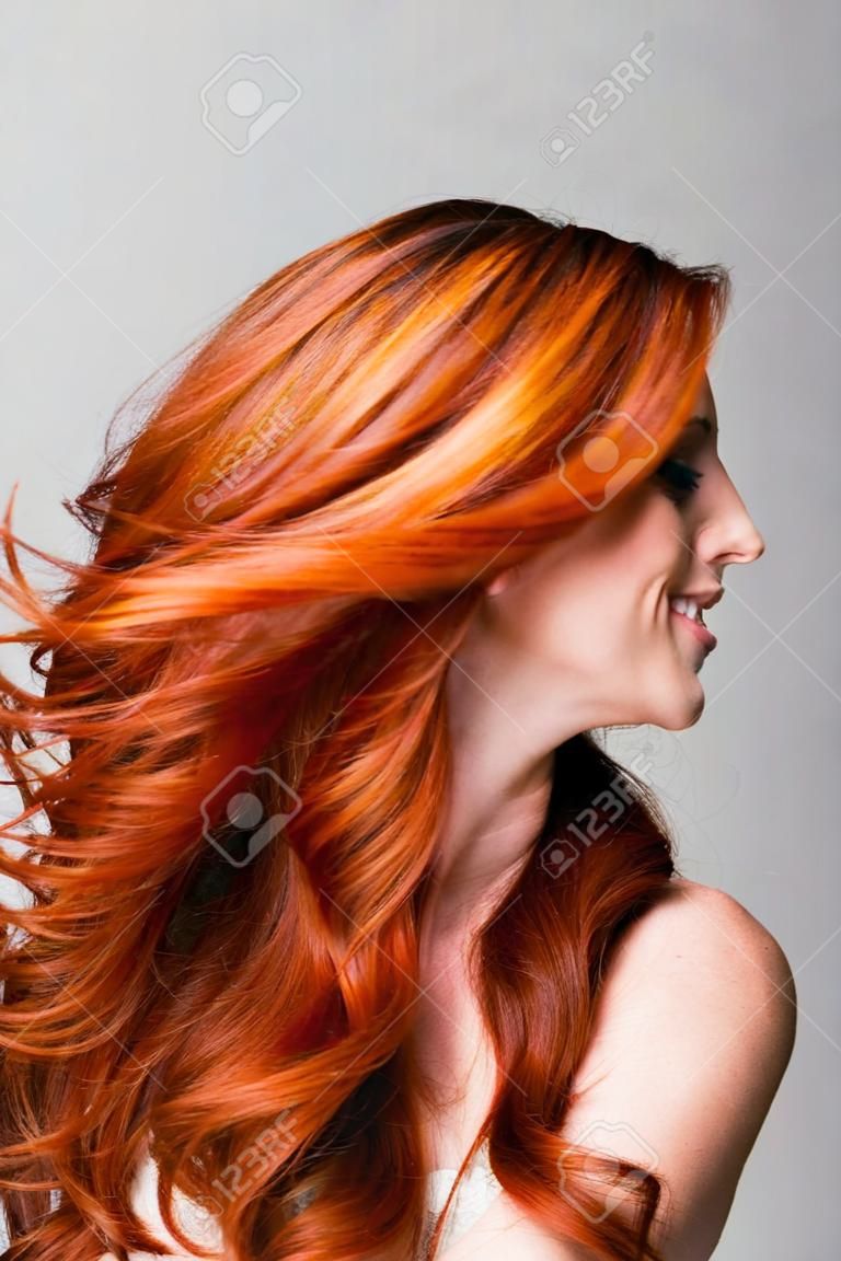 Profilo di una donna fresca rossa lanciare il suo splendido lunghi capelli ondulati in modo che sta volando sciolti intorno al viso