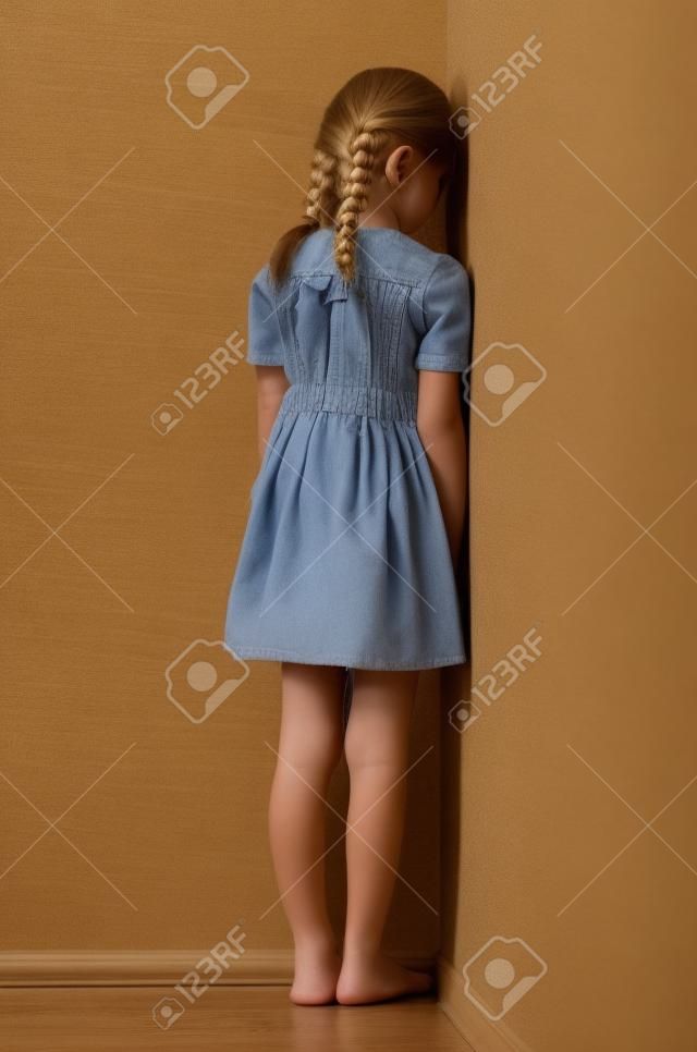 小女孩和她的金发辫子站在对着墙生闷气或为罪孽的角落