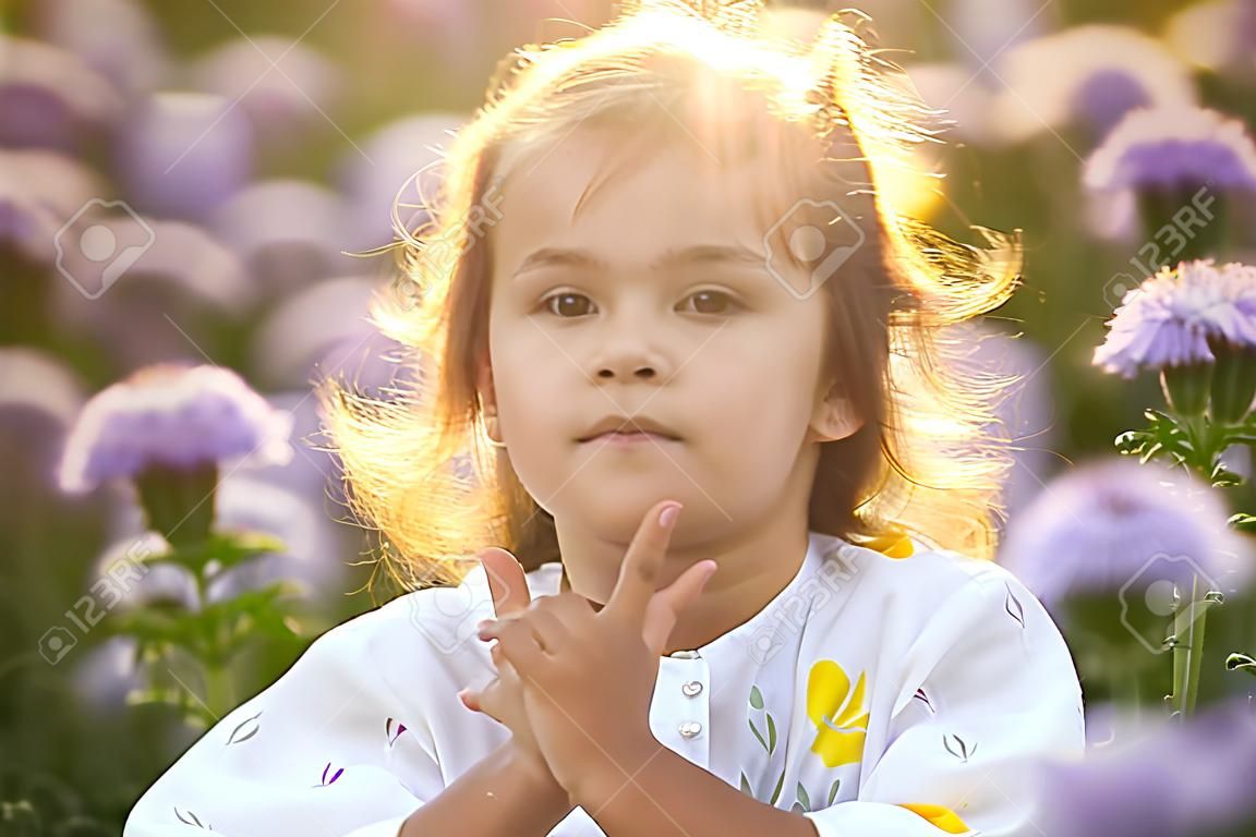 Close-up Portret van een klein schattig meisje dragen witte jurk in de paarse facelia bloemen veld bij zonsondergang