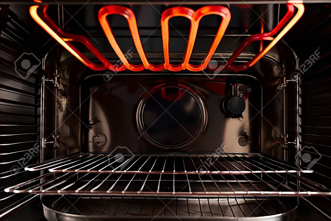 Olhando para dentro do forno de cozinha vazio preto. Há uma prateleira de treliça e um elemento de aquecimento quente vermelho. fundo.