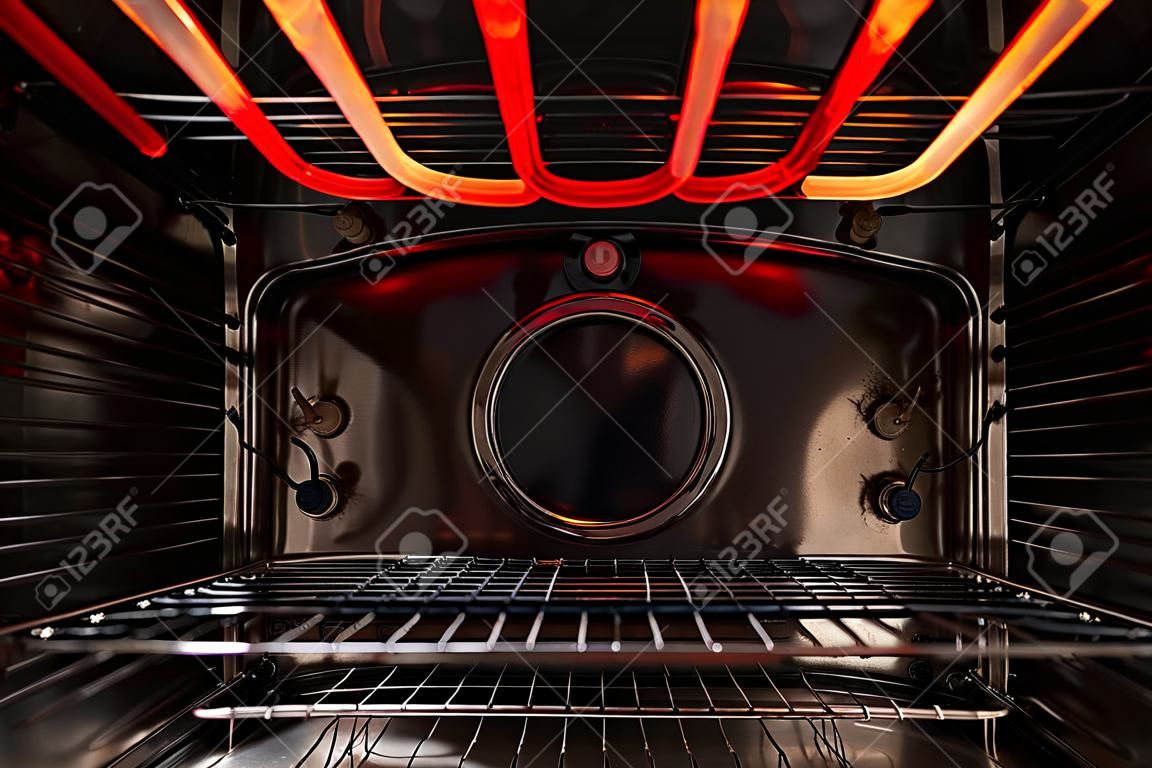 Olhando para dentro do forno de cozinha vazio preto. Há uma prateleira de treliça e um elemento de aquecimento quente vermelho. fundo.