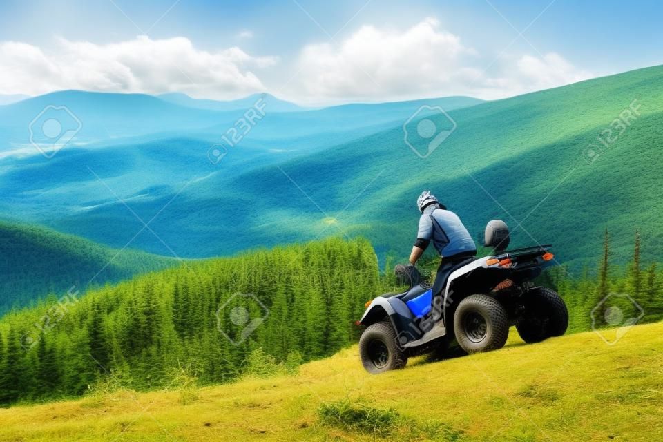 Mężczyzna jedzie w dół na ATV górkowata droga na tle góry, las i niebieskie niebo. Koncepcja aktywnego wypoczynku w górach