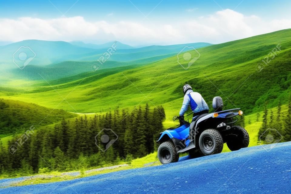 Mężczyzna jedzie w dół na ATV górkowata droga na tle góry, las i niebieskie niebo. Koncepcja aktywnego wypoczynku w górach