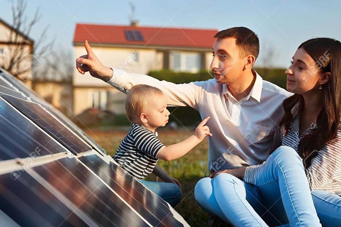 Homem mostra a sua família os painéis solares na trama perto da casa durante um dia quente. Jovem mulher com uma criança e um homem nos raios de sol olhar para os painéis solares.