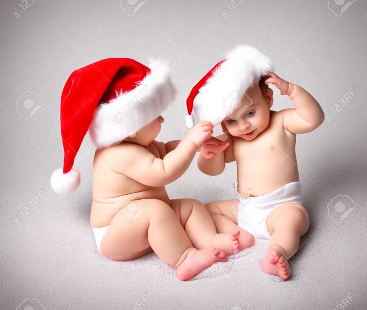 Babies in diapers playing with Santa hats