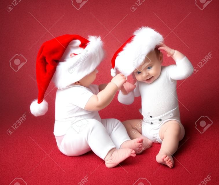 Babies in diapers playing with Santa hats