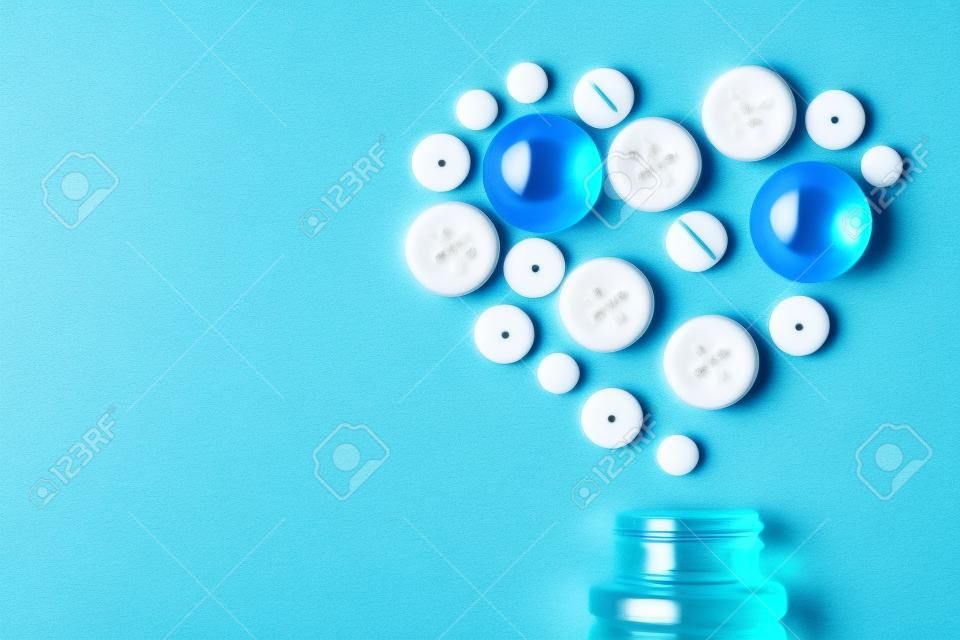 Medical concept - heart made of white pills of different size with bottle on blue background, top view