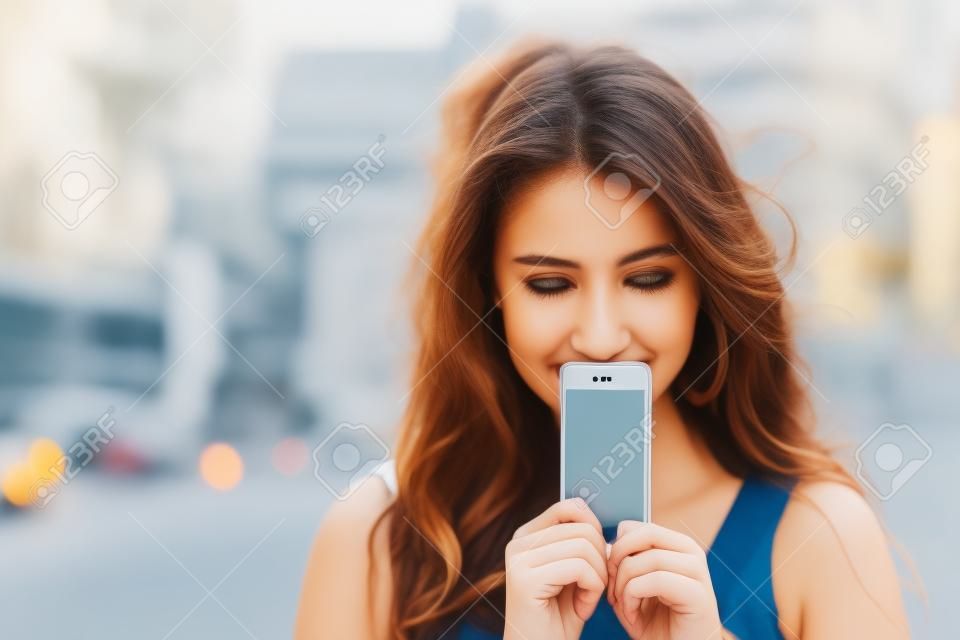 Mujer joven cubre la cara smartphone de pantalla sobre un fondo de la calle del verano