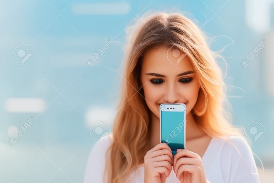 Молодая женщина охватывает ее лицо экрана смартфона на фоне летнего улице