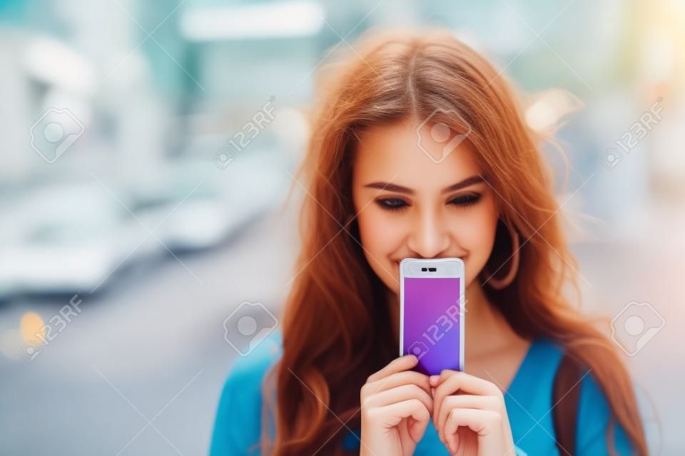 Fiatal nő eltakarja arcát képernyős okostelefon a háttérben nyári utcai