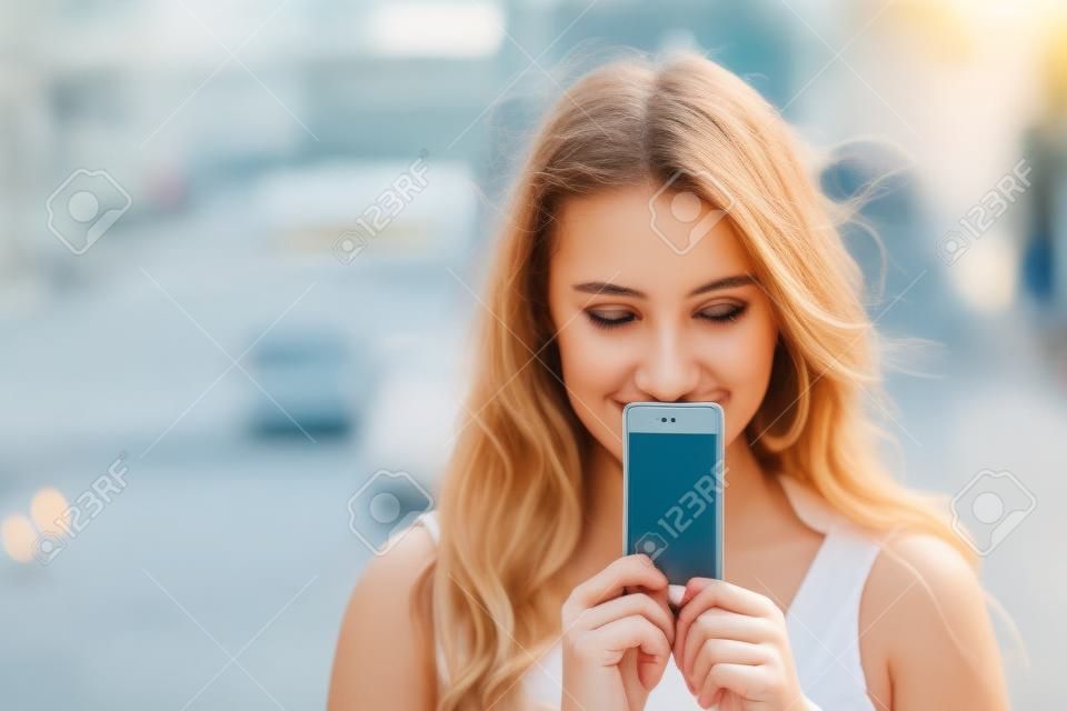 Молодая женщина охватывает ее лицо экрана смартфона на фоне летнего улице