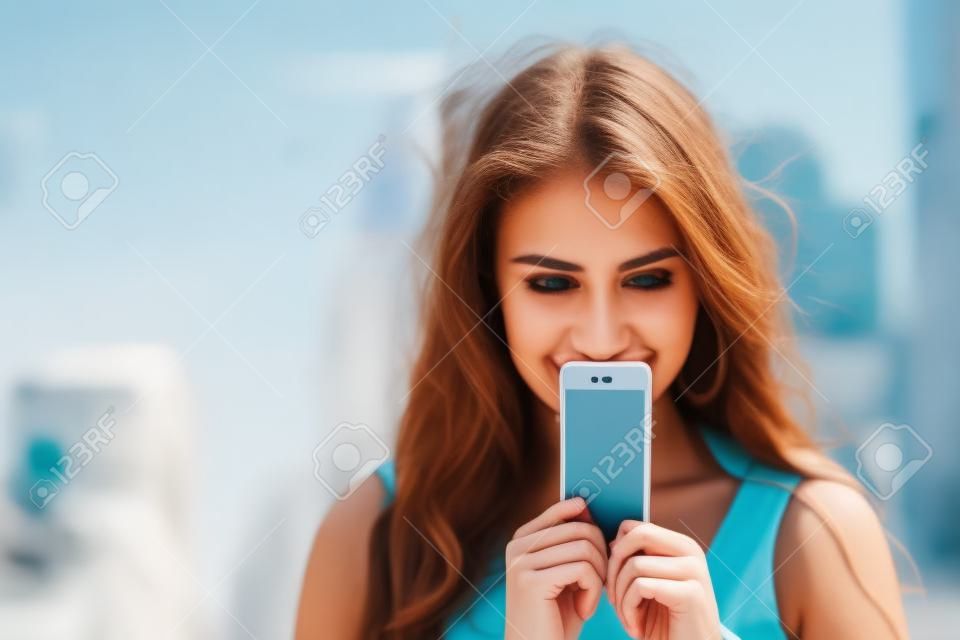 Young woman covers her face screen smartphone on a background summer street