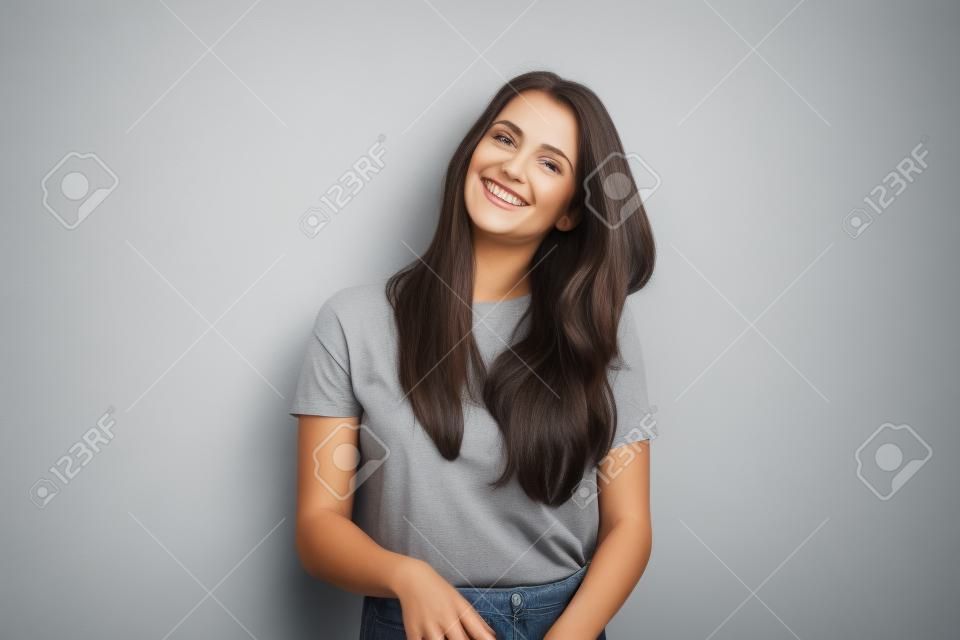 Glückliche schöne Brunettefrau im grauen T-Shirt, lokalisiert auf weißem Wandhintergrund