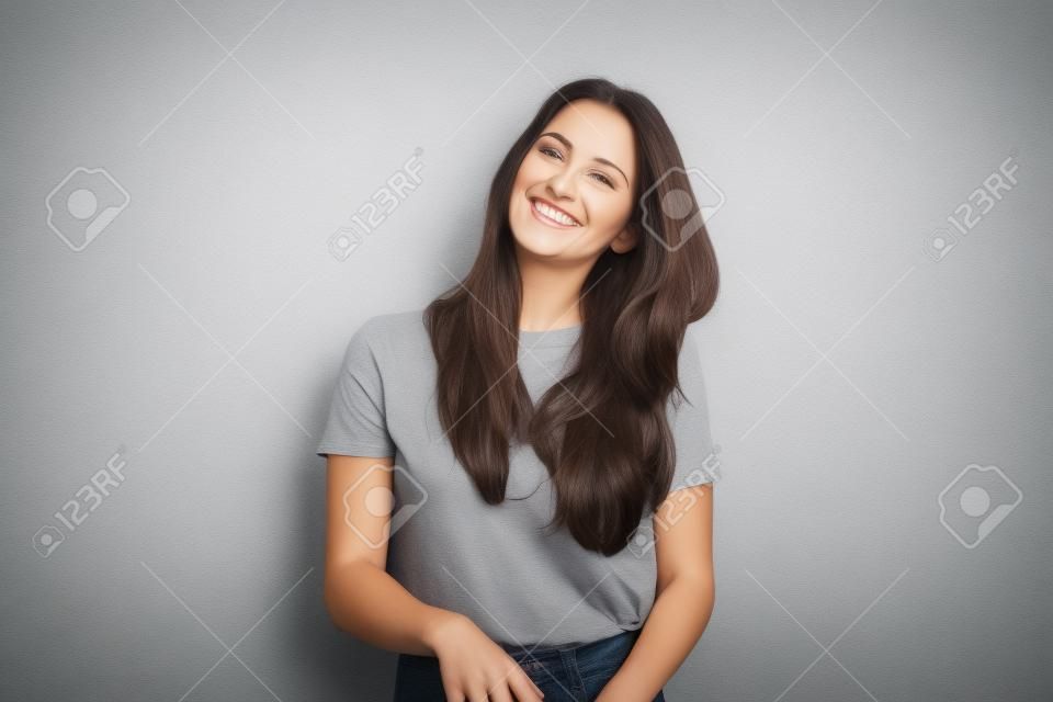 Feliz hermosa mujer morena en camiseta gris, aislada en el fondo de la pared blanca