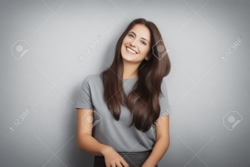 Feliz hermosa mujer morena en camiseta gris, aislada en el fondo de la pared blanca