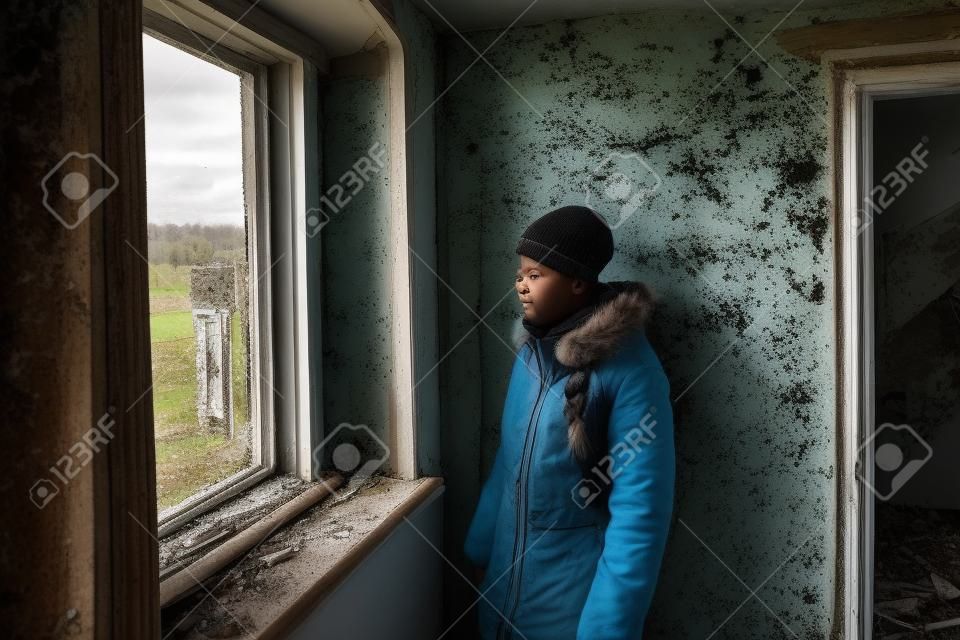 Een tiener kijkt uit het raam in een verlaten en geruïneerd huis