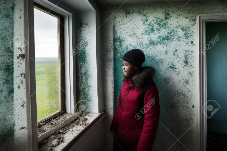 A teenager looks out the window in an abandoned and ruined house