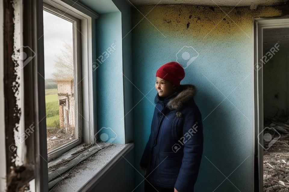 A teenager looks out the window in an abandoned and ruined house