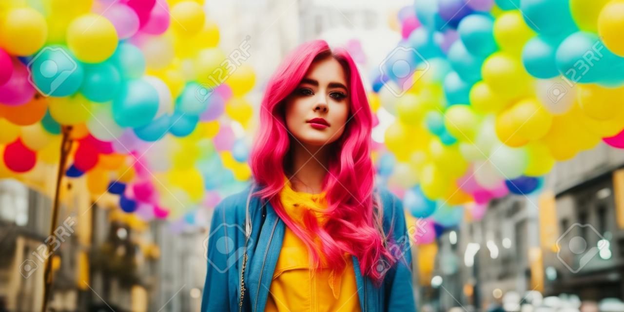 Giovane bella donna hipster in giacca gialla in posa in strada cittadina con palloncini colorati