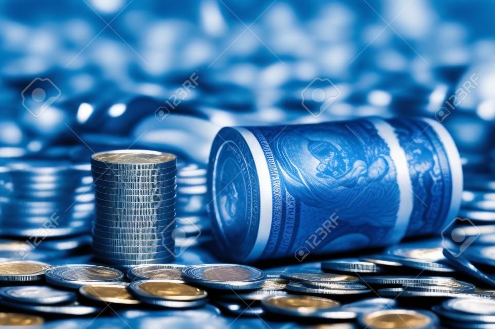 A roll of dollars with coins on the background of scattered one hundred dollar bills in blue light