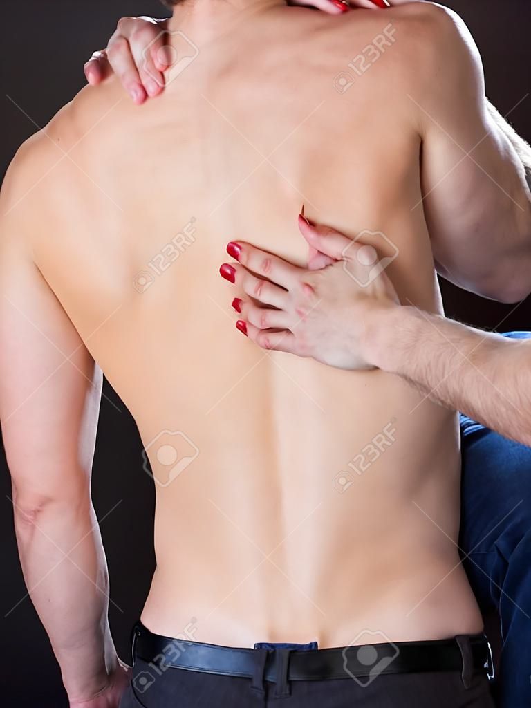 Main grattant le dos de l'homme torse nu de femme passionnée sur fond noir