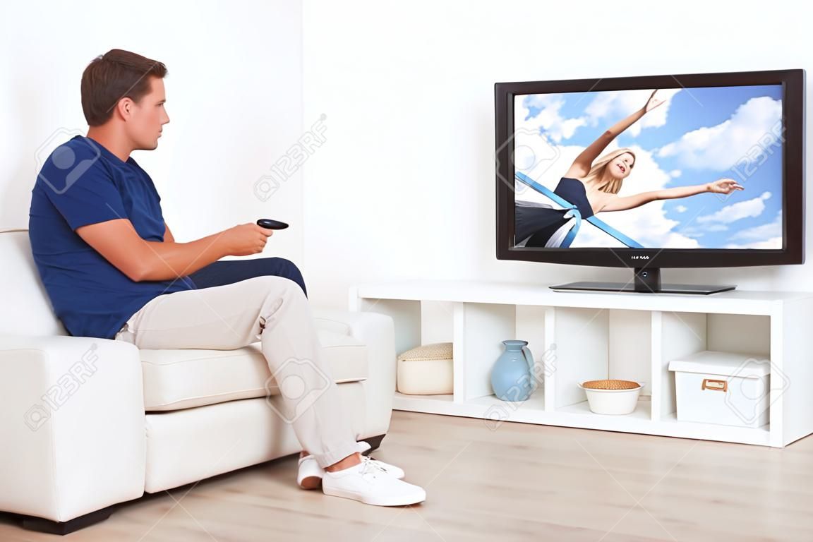 Longitud total de hombre viendo la televisión en la sala de estar en casa