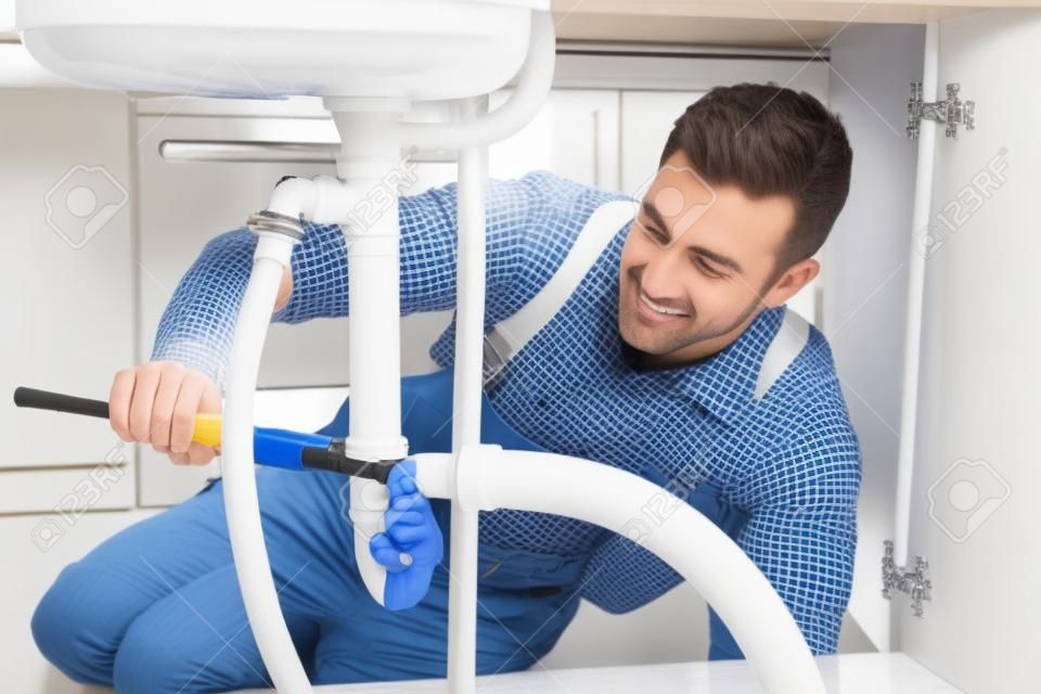 Fontanero sexo masculino que repara el fregadero blanco de tuberías en la habitación Cocina