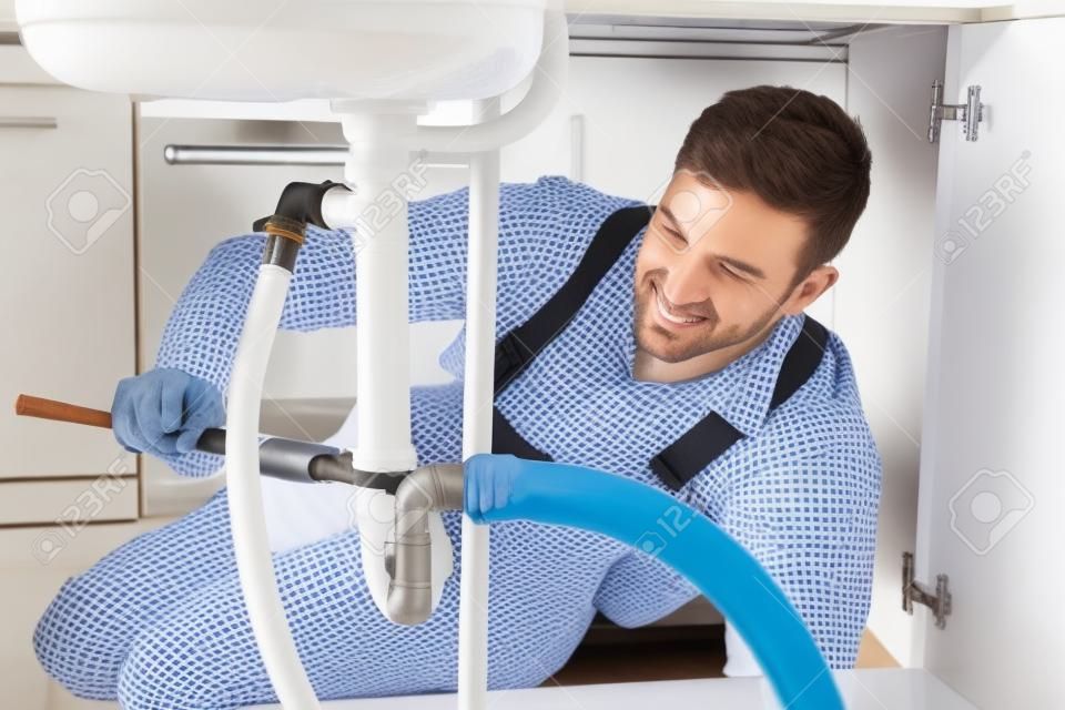 Fontanero sexo masculino que repara el fregadero blanco de tuberías en la habitación Cocina