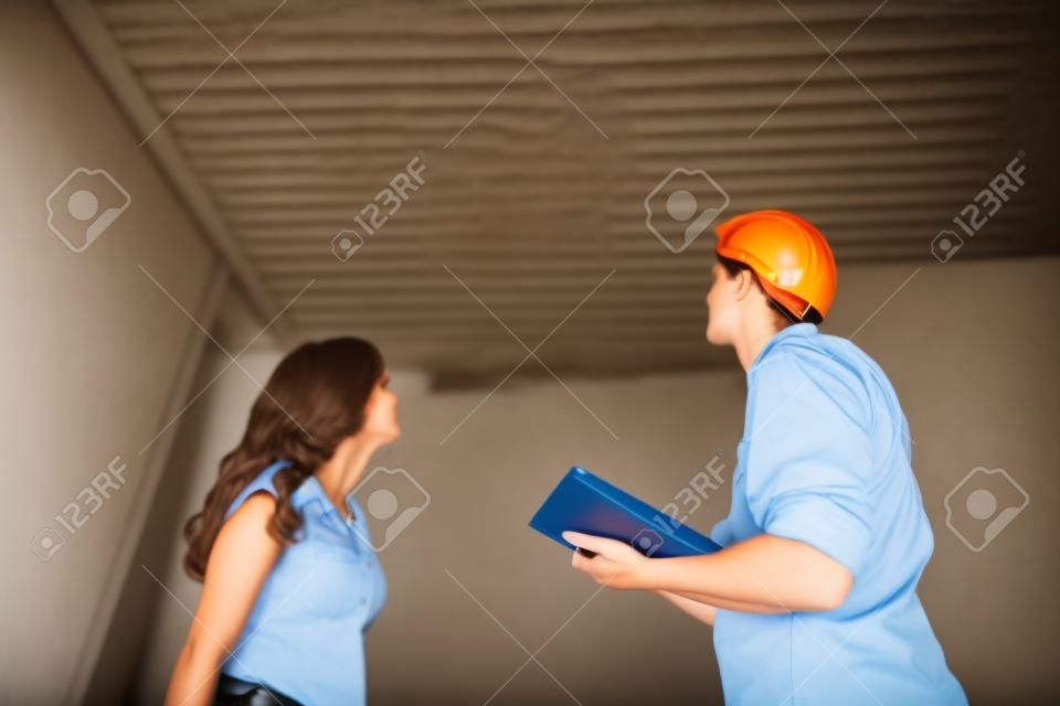 Young Worker Writing On Clipboard With Woman Standing In House