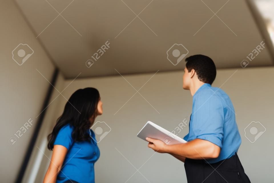 Young Worker Writing On Clipboard With Woman Standing In House