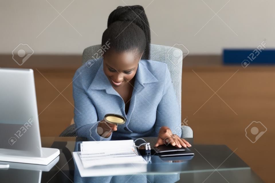 Afrikanische Geschäftsfrau, die Rechnung durch Lupe betrachtet