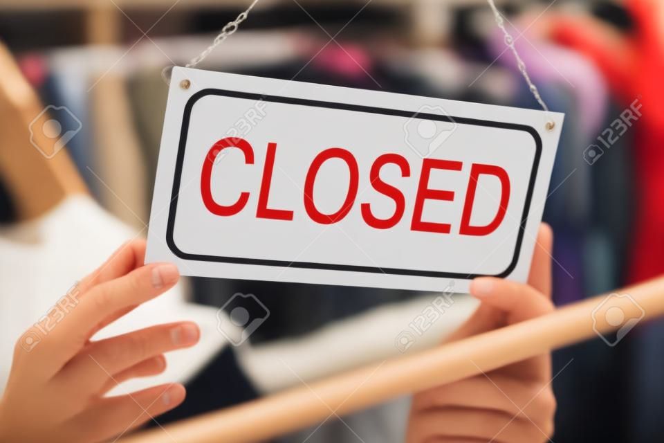 Closeup of female owner holding closed sign in clothing store