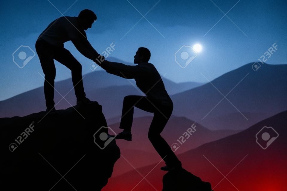 Silhouette giovane uomo assistere amico di sesso maschile in arrampicata su roccia