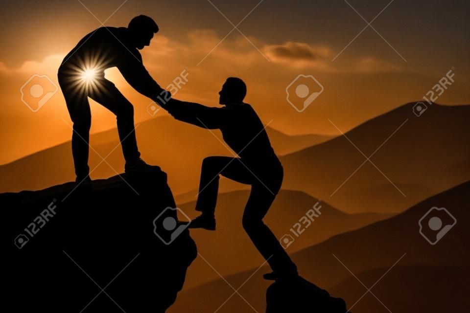 Silhouette young man assisting male friend in climbing rock